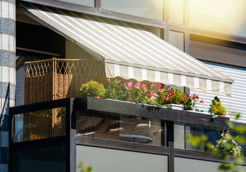 French balcony with beautiful awning and flowers covered with rays of sun - protection during hot weather and radiation